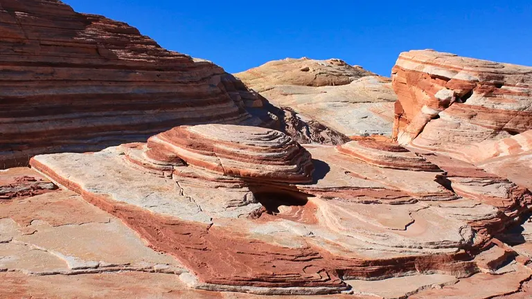 Striated red and beige rock formations under a clear blue sky at Valley of Fire State Park