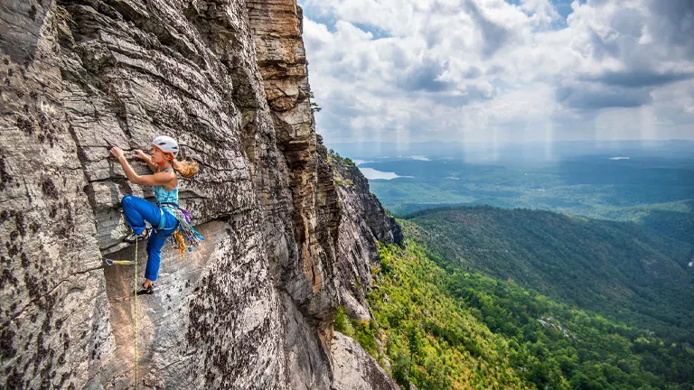 a climber, equipped with safety gear, scaling a steep and rugged cliff in Pisgah National Forest
