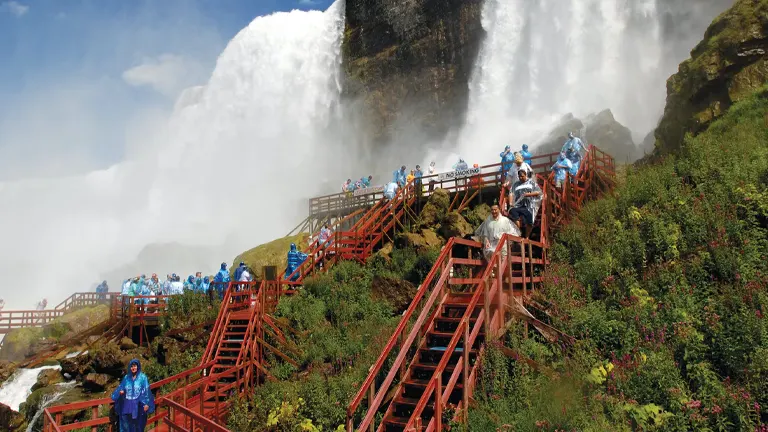 Visitors in blue ponchos exploring Niagara Falls State Park via red wooden staircases amidst misty falls