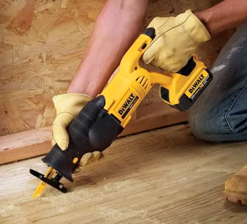 A person using a yellow and black DeWalt reciprocating saw to cut through wood