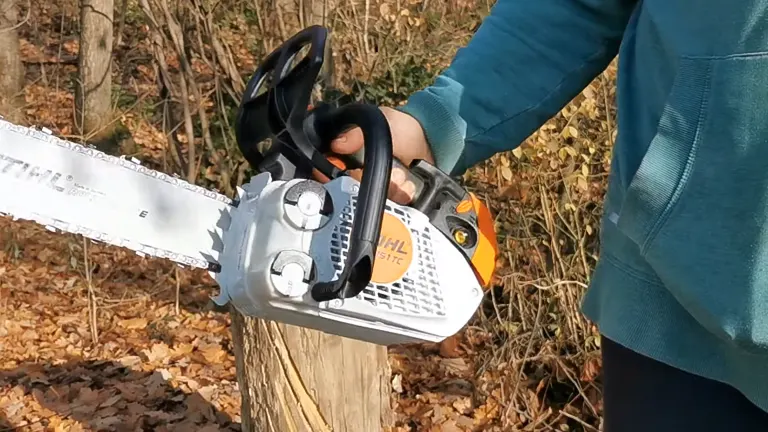 Person in teal shirt holding a Stihl MS 151 TC E Chainsaw, preparing to cut a tree stump