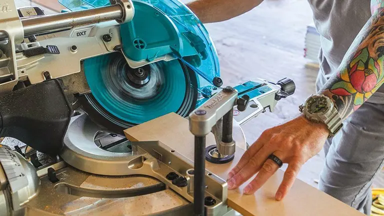 A person using a Makita 36V LXT Brushless 12" Dual-Bevel Sliding Compound Miter Saw with Laser Kit to cut wood in a workshop