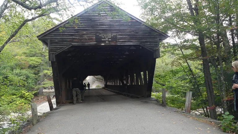 A wooden covered bridge in White Mountain National Forest surrounded by lush greenery