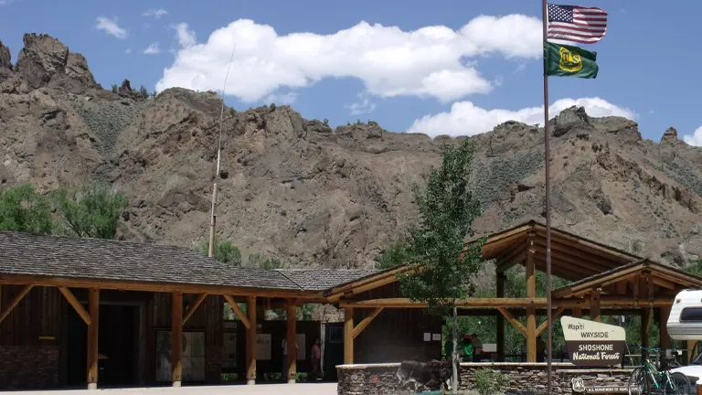 Visitor center at Shoshone National Forest with the American and forest flags flying, set against a rocky mountain backdrop