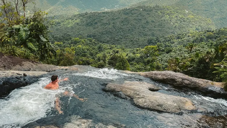 A person enjoying a natural pool amidst the lush greenery of El Yunque National Forest