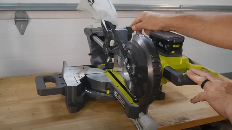 A Ryobi PBT01B ONE+ 18V 7-1/4” Sliding Compound Miter Saw on a workbench with a person’s hands adjusting it
