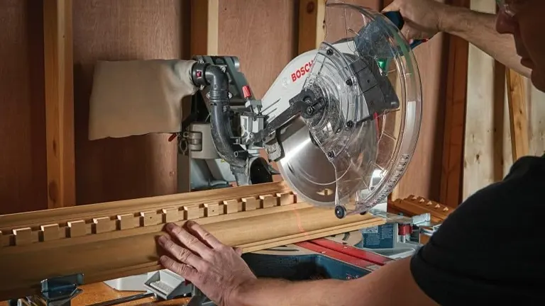 Person using a BOSCH PROFACTOR 18V 12" Dual-Bevel Glide Miter Saw to cut a wooden plank in a workshop