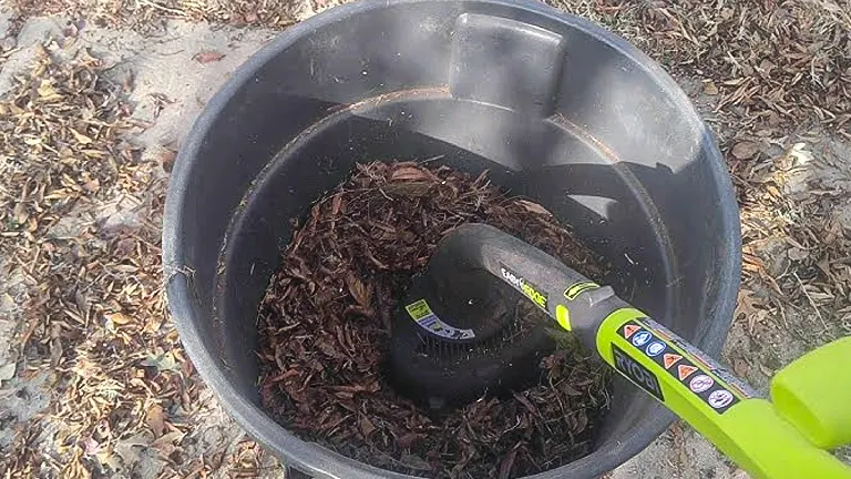 Person using a green leaf blower to gather mulch into a large black container