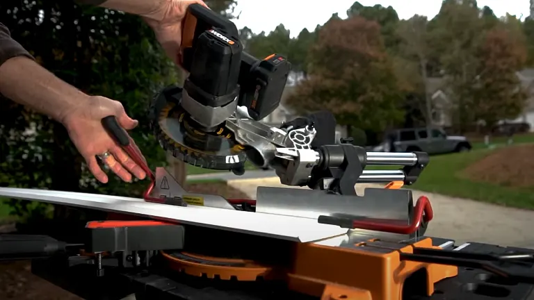 A person using a WORX WX845L 20V 7.25” Power Share Cordless Sliding Compound Miter Saw to cut wood on a workbench, with a suburban neighborhood in the background