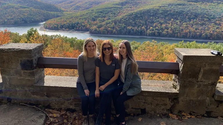 Three people overlooking the colorful autumn foliage in Allegheny National Forest from a stone wall