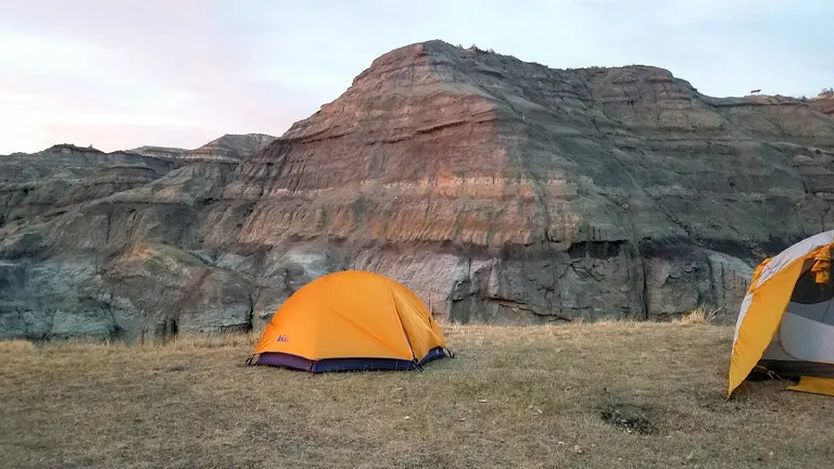 Camping tents at the base of rugged terrains in Makoshika State Park during sunset
