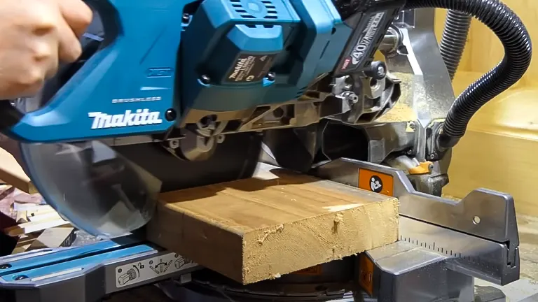 Blue and black Makita 40V Max XGT 8-1/2” Dual-Bevel Sliding Compound Miter Saw cutting a wooden plank in a workshop