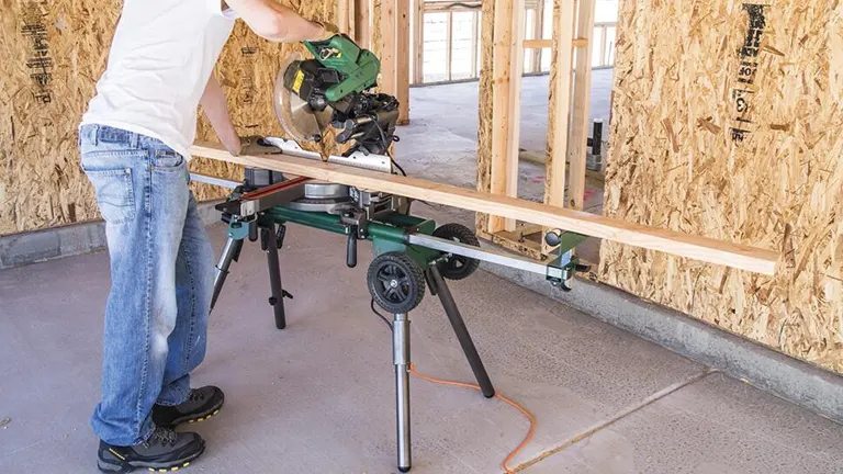 Person using a green Masterforce Universal Folding Miter Saw Stand with Wheels at a construction site