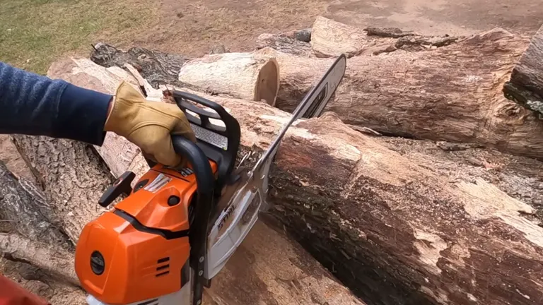 a person, visible from the elbow down, using a Stihl MS 500i Chainsaw to cut through a large piece of wood