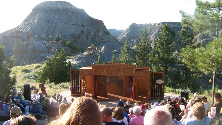 Audience watching a performance at an outdoor theater in Makoshika State Park with rugged terrains and greenery in the background