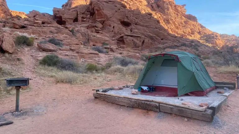 A tent pitched near a grill at a campsite in Valley of Fire State Park with red rocky terrain in the background
