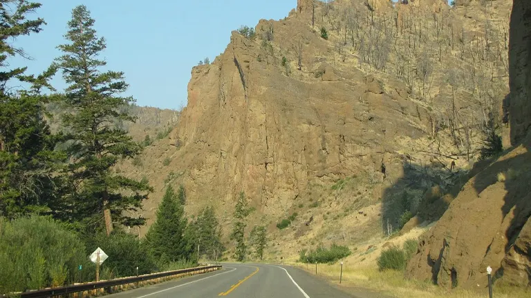 Scenic drive through Shoshone National Forest with towering rocky cliffs and lush greenery