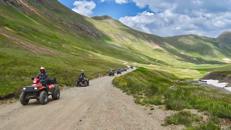 Riders on ATVs following a trail through a scenic mountain landscape