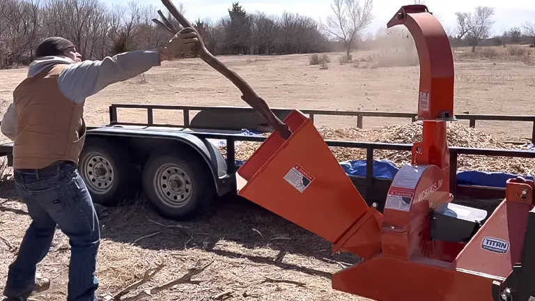 Person feeding a branch into a Titan Attachments 40 HP 3-Point Wood Chipper in an open field