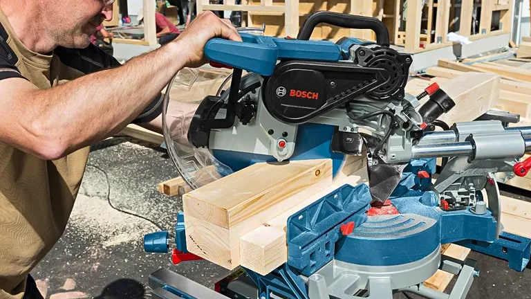 Person using Bosch GCM12SDE 12” Professional Glide Miter Saw to cut wood at a construction site