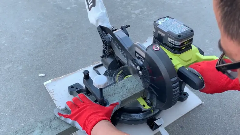 Person in red gloves using a black and green Ryobi P553 18V ONE+ 7-1/4” Compound Miter Saw on a workbench