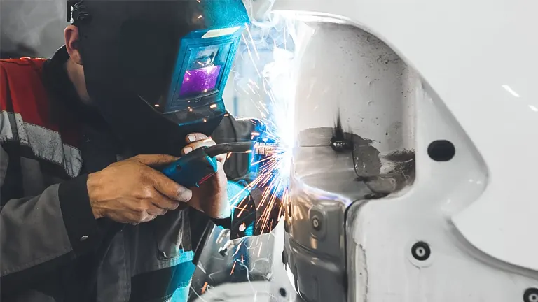 Welder in safety gear using a MIG welder on a metal object, surrounded by bright sparks