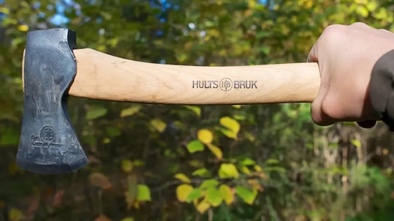 Person holding a Hults Bruk camping hatchet with a wooden handle and metal head, outdoor