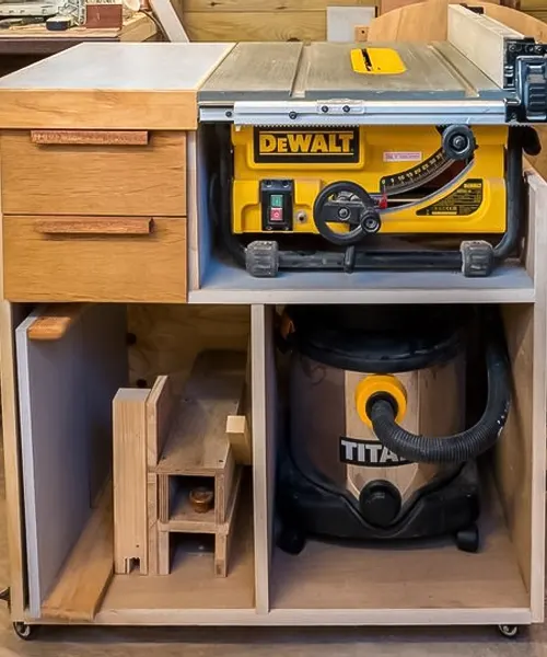 DEWALT DW745 table saw embedded within a custom wooden workbench with built-in storage. A TITAN vacuum cleaner is stored in an open cabinet space below the table saw