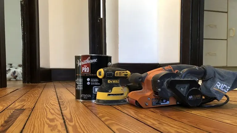 Belt sander, varnish, and gloves on a newly refinished hardwood floor