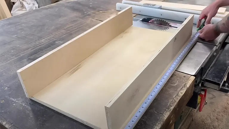 Wooden box joint jig on table saw with hand holding pencil