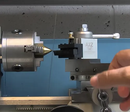 Hand adjusting a knob on a blue wood lathe in a workshop