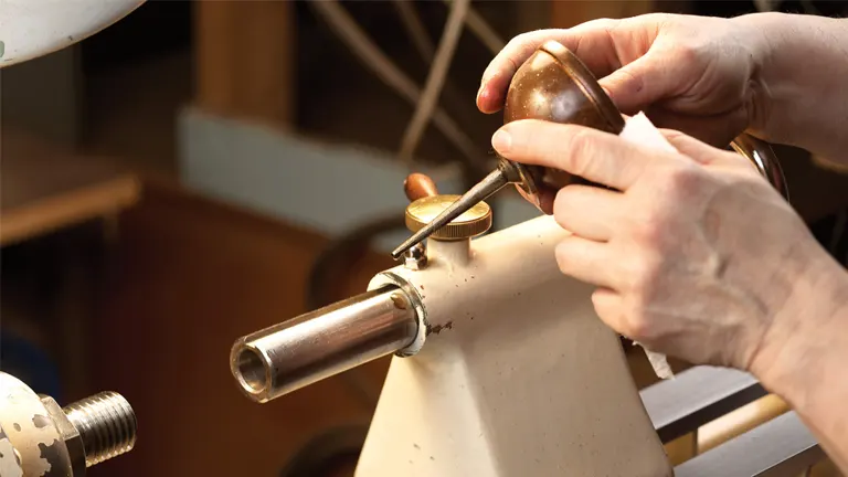 Hand using a wood lathe tool on a white lathe machine in a workshop