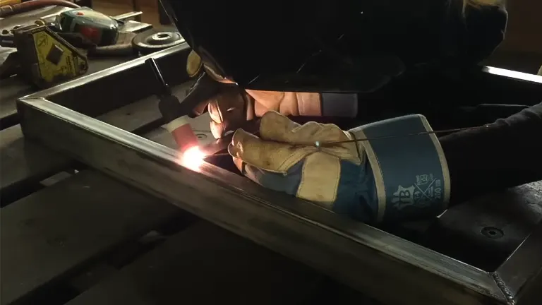 A person welding a metal frame in a workshop using an Everlast Power 185DV AC/DC TIG Stick Welder