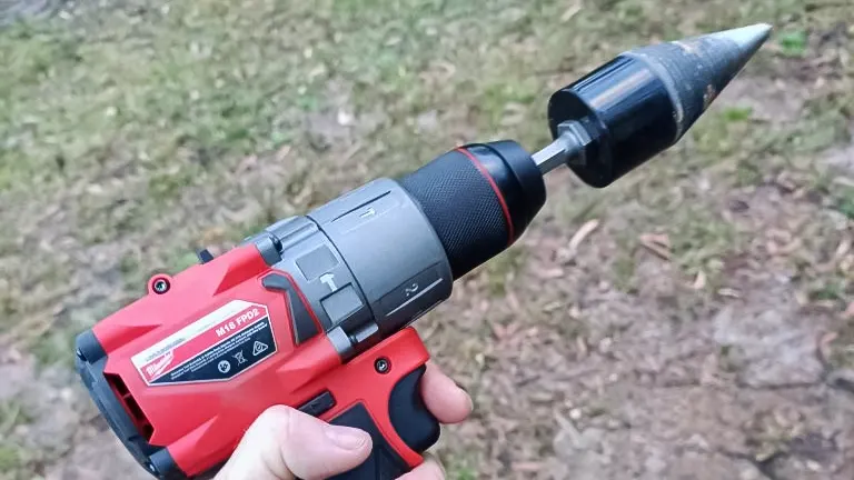 Hand holding a red and black drill with a firewood log screw splitter drill bit attached in an outdoor setting