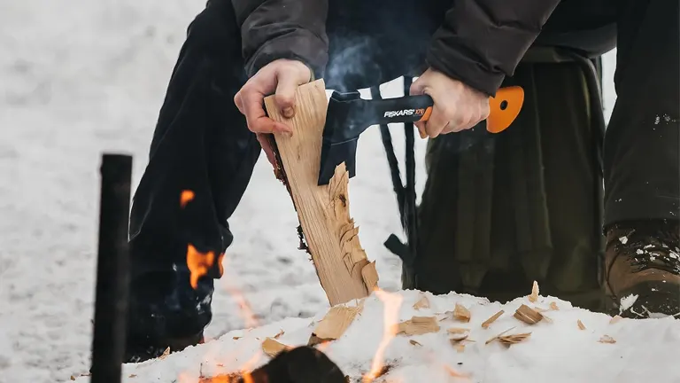 Person splitting wood with a Fiskars X7 hatchet near a fire