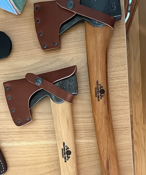 Two Gransfors Bruks Wildlife Hatchets with leather sheaths on a wooden surface