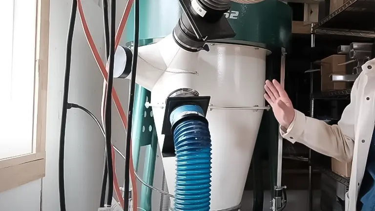 Person inspecting a Grizzly 3 HP Portable Cyclone Dust Collector in a workshop with shelves and electrical cables in the background
