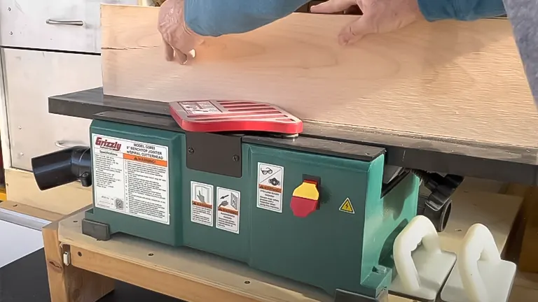 Person using a green Grizzly Industrial G0945 6-inch Benchtop Jointer to process a large wooden plank in a workshop