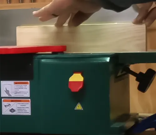 Person using a green Grizzly Industrial G0945 6-inch Benchtop Jointer in a workshop