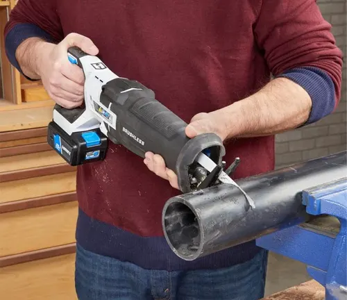 Person in red sweater using a HART 20-Volt Reciprocating Saw to cut through a metal pipe in a workshop