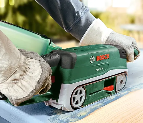 Person using a green Bosch belt sander on a wooden floor outdoors
