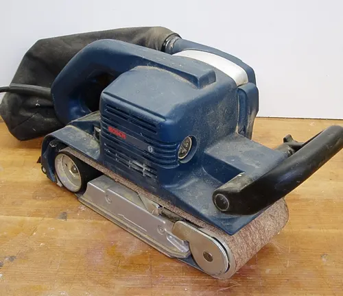 Blue and black belt sander on a wooden surface with sawdust