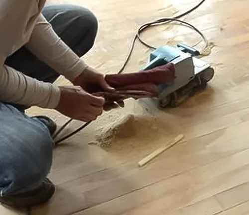 Person using a belt sander on an unfinished wooden floor