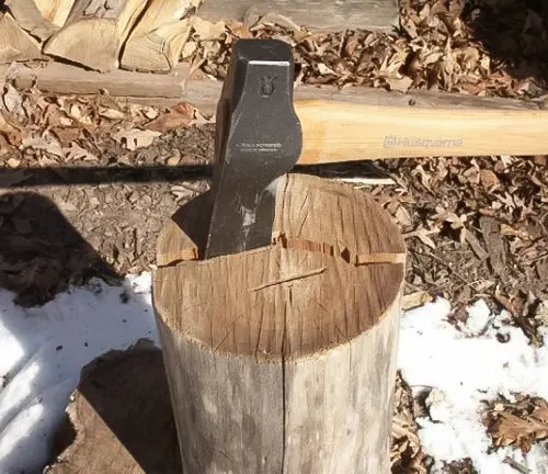 Husqvarna S21 Wooden Handle Splitting Maul embedded in a wooden log outdoors, surrounded by chopped wood and snow