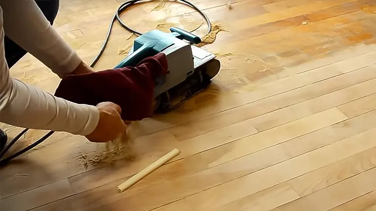 Person sanding a hardwood floor with a light blue sander
