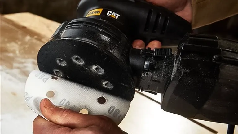 Hand holding a CAT brand sander with a white sanding disc