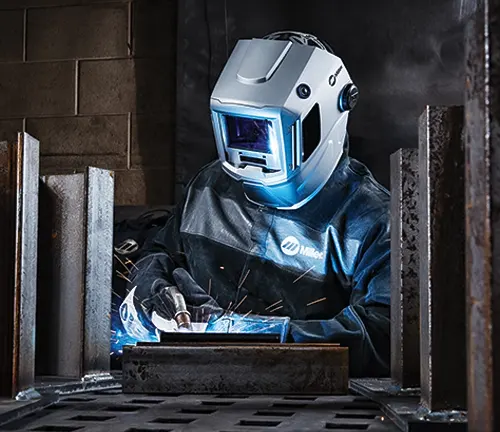 Welder in comprehensive safety gear actively working in an industrial setting, illuminated by the bright blue light of the welding process