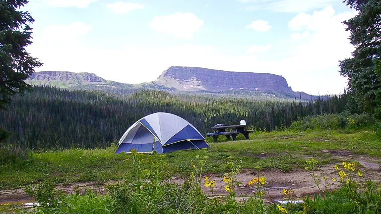 peaceful camping scene with a tent and a picnic table set against the backdrop of lush greenery and towering mountains