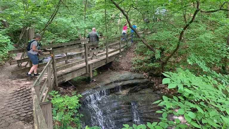 hikers on a wooden bridge observing a small waterfall