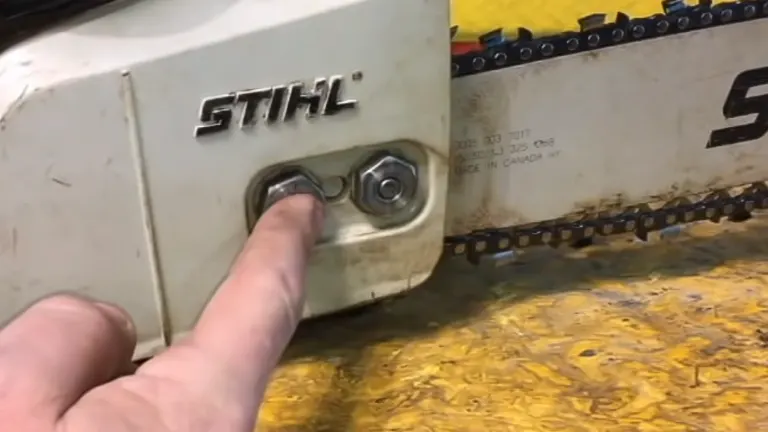 person’s finger pointing at the bar nuts on a STIHL chainsaw, indicating the process of loosening them